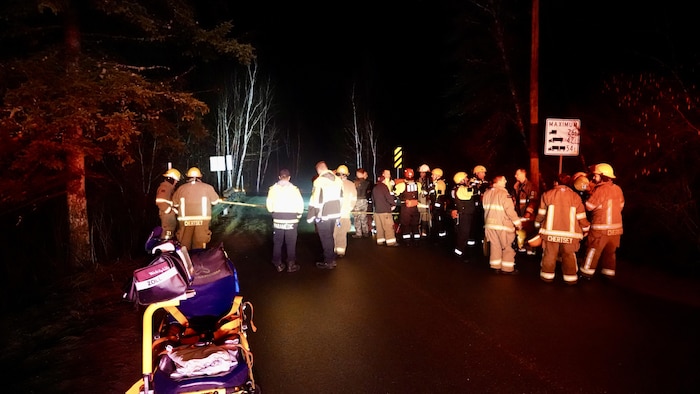 Plusieurs pompiers sont debout sur une route pendant la nuit à l'intérieur et à l'extérieur d'un périmètre de sécurité.