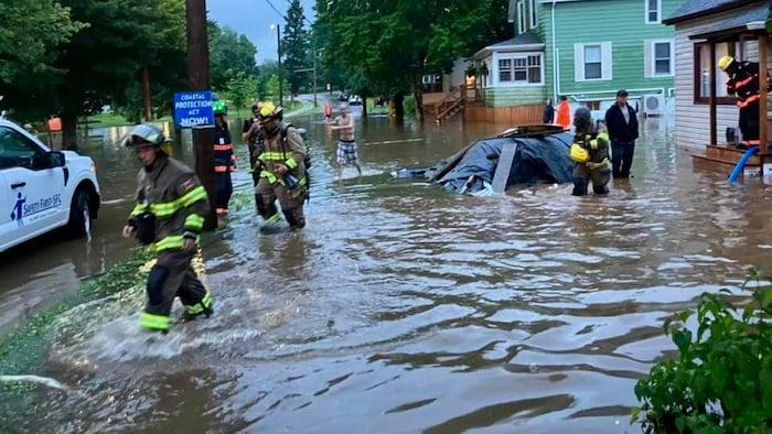 Des pompiers progressent dans une rue résidentielle inondée, sous plusieurs dizaines de centimètres d'eau.