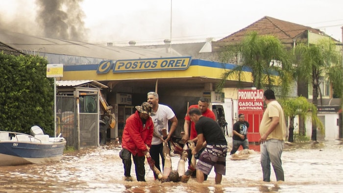 Des hommes portent un homme blessé dans une rue inondée, avec, en arrière-plan, un panache de fumée.