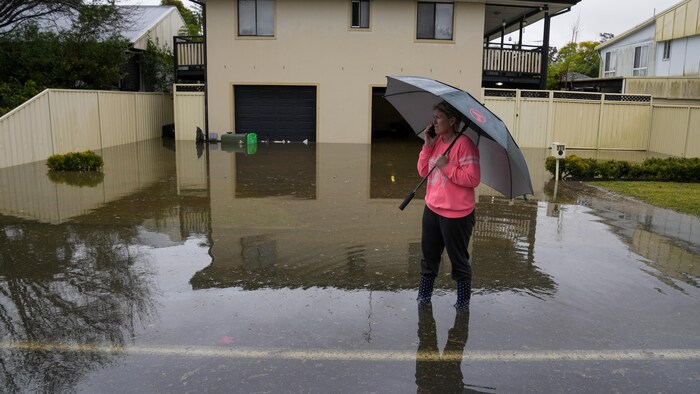 Une femme se trouve dans l'entrée de garage d'une maison inondée. L'eau atteint ses mollets. 