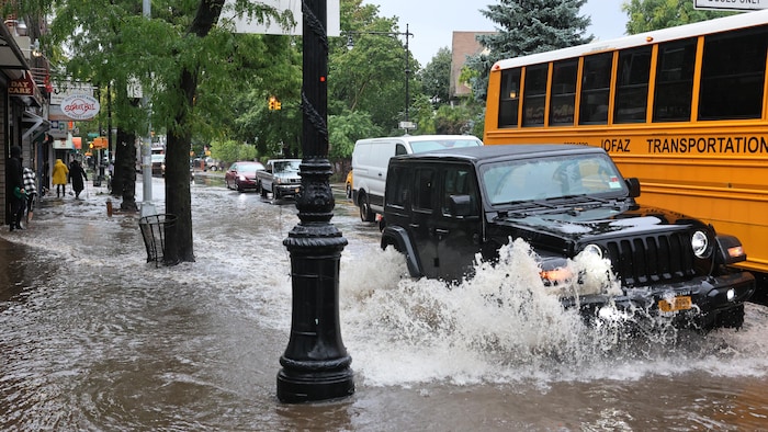 Des voitures et un autobus circulent dans une rue submergée.
