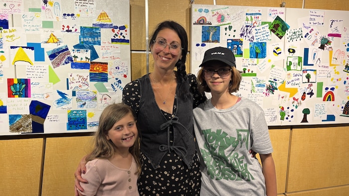 Alice Gagné (gauche) sa maman, Caroline Dubé (centre) et sa sœur, Mia Gagné souriantes devant des fresques colorées.
