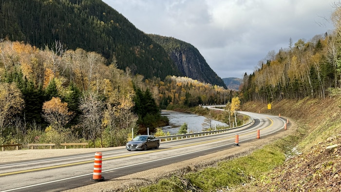 Une voiture grise circule sur une route sinueuse bordée de cônes orange.