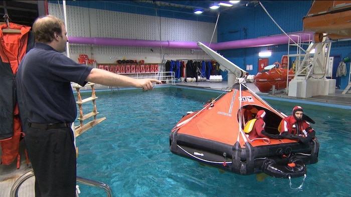 Des étudiants participant à une formation de sauvetage en mer prennent place à bord d’un radeau de survie gonflable déployé dans une piscine intérieure. 