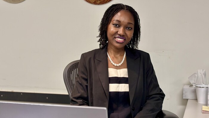 Une jeune femme assise devant un ordinateur sourit à la caméra.