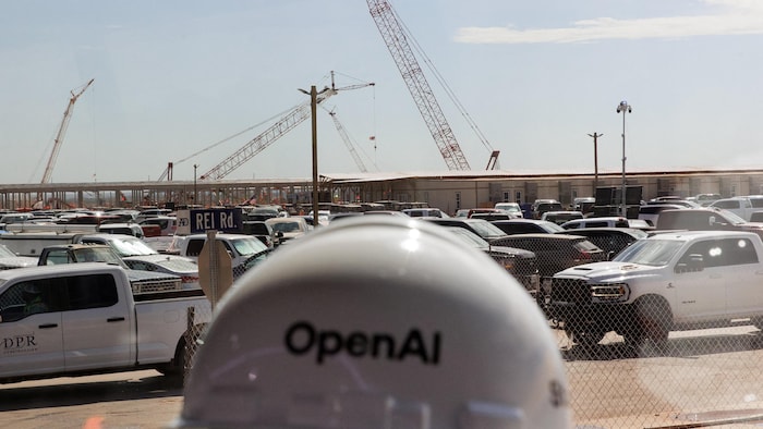 La structure métallique des centres de données en construction en arrière-plan d'un casque à l'effigie d'OpenAI.