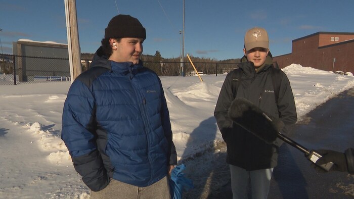 Deux jeunes répondent aux questions d'une journaliste, près d'une école, à l'extérieur.