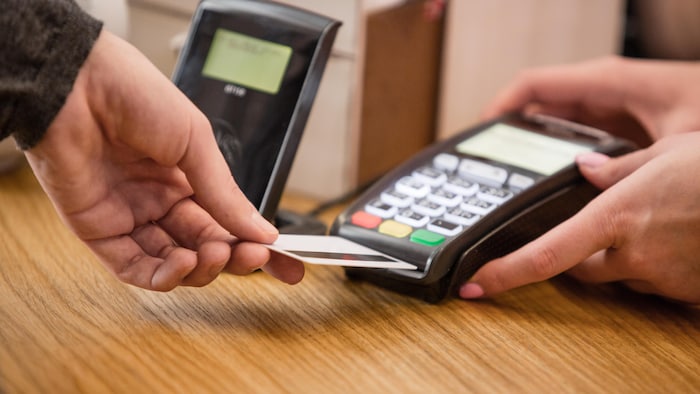 Une personne tend sa carte vers une machine à paiement direct.