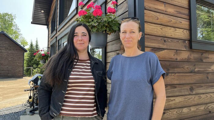 Deux femmes posent l'une à côté de l'autre devant une maison.