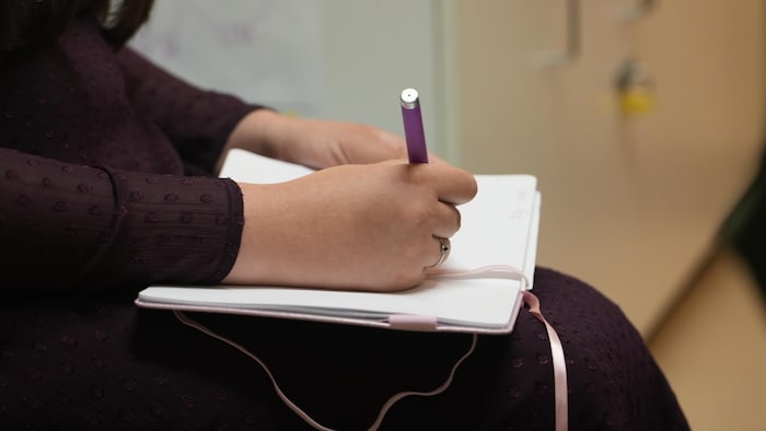 Un cahier posé sur des genoux. Une main qui tient un crayon pour écrire dans le cahier.