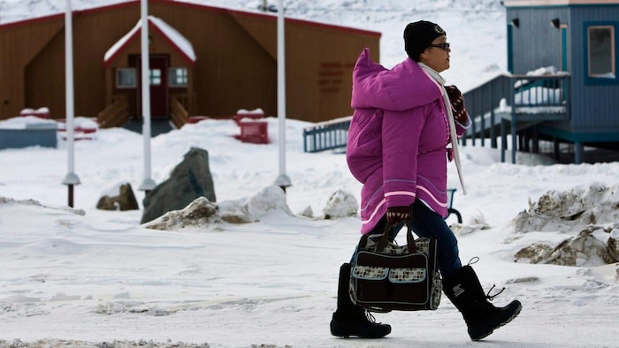 Une femme portant un parka traditionnel marche sur la rue en hiver.