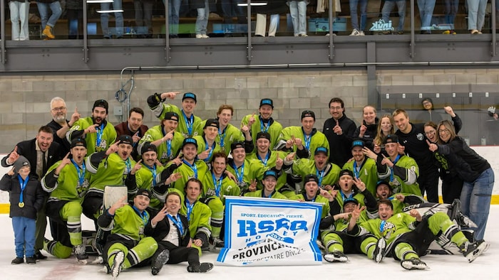 Une équipe de hockey en uniforme vert lime célèbre une victoire sur la glace. Les joueurs portent des médailles et posent derrière une bannière du RSEQ. Des partisans les observent et les applaudissent depuis les gradins en arrière-plan.