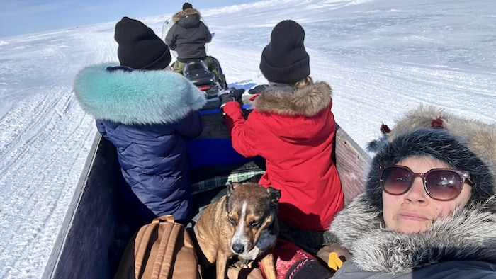 Une femme et ses enfants sont assis dans un qamutik, un traîneau conçu pour se déplacer sur la neige et sur la glace, tiré par une motoneige.