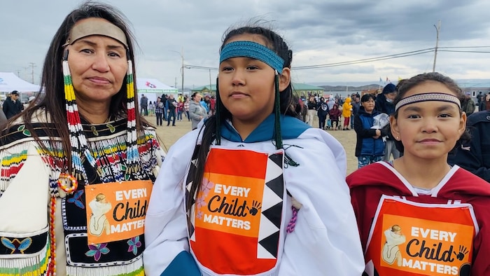 Une femme avec deux petites filles en tenues traditionnelles inuit et portant l'inscription chaque enfant compte.