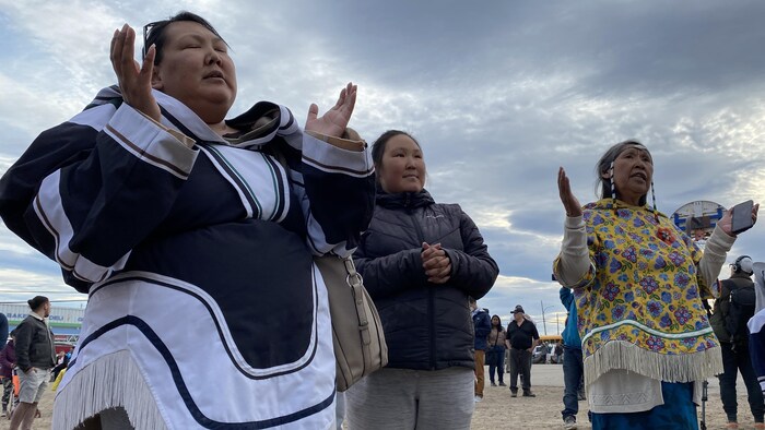 Des femmes inuit ont les mains en l'air pour prier et ferment les yeux.