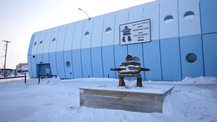 Un inuksuk enneigé devant le bâtiment d'une école secondaire, à Iqaluit.