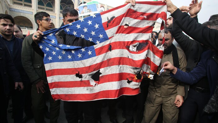 Des hommes en colère enflamment un drapeau.