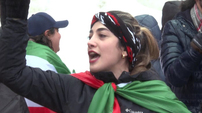 Une femme de profil en train de crier. Elle a un drapeau de l'Iran noué autour du cou.