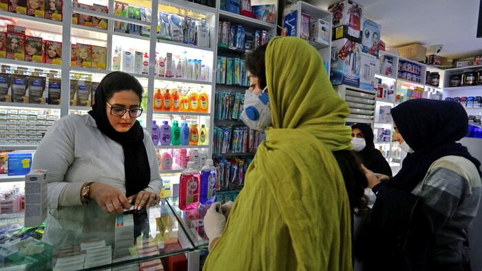Des clientes portant un masque sont au comptoir d'une pharmacie.