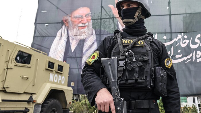 Un membre des forces de sécurité iraniennes monte la garde à côté d'une banderole géante honorant l'ancien guide suprême iranien, l'ayatollah Ali Khamenei, à Téhéran, le 31 mars 2026.
