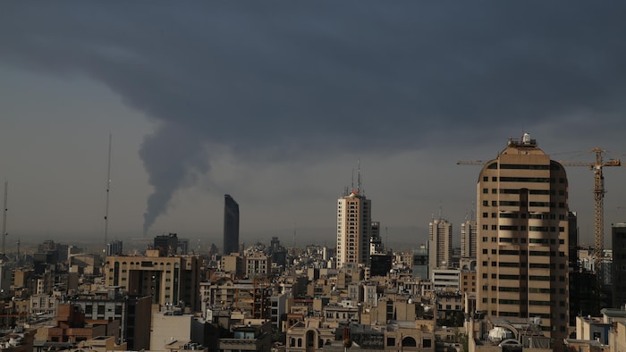 Black clouds rise in the gray sky of a city.