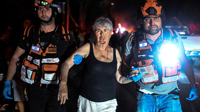 Une femme blessée est soutenue par deux secouristes. 