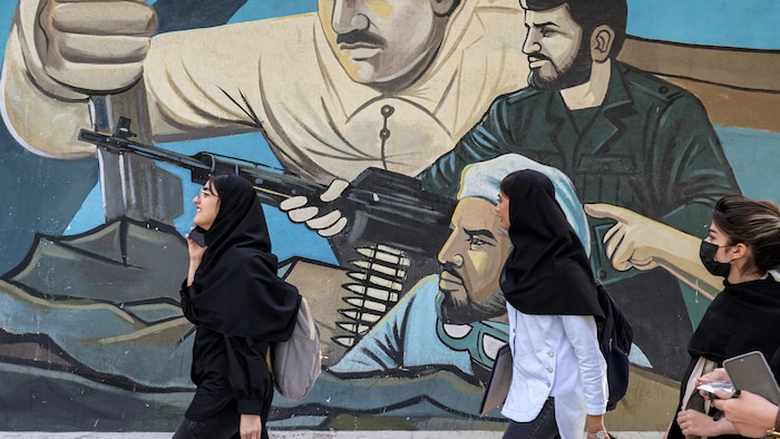 Des personnes marchent devant une murale représentant des combattants armés de fusils d'assaut.