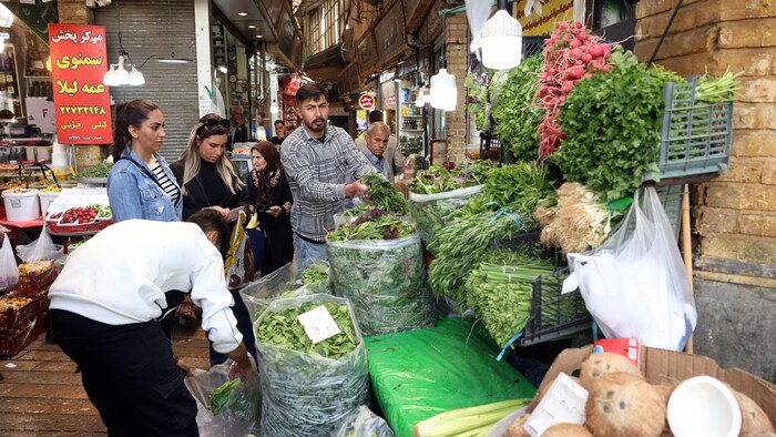 Deux jeunes femmes autour d'un étal de légumes dans un marché.