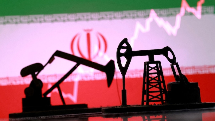 Des représentations de puits de pétrole imprimées en 3D devant un drapeau iranien.