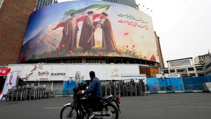 Un homme à moto regarde un grand panneau d'affichage représentant le nouveau guide suprême iranien Mojtaba Khamenei, à Téhéran.