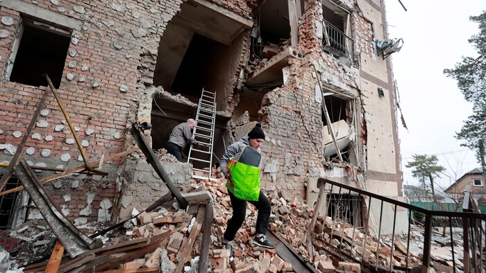 Une femme transporte un sac dans les ruines d'un immeuble éventré.