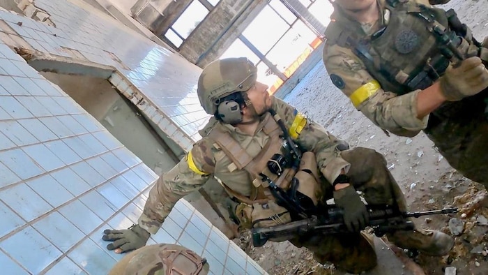 Deux soldats sont accroupis dans un bâtiment endommagé.