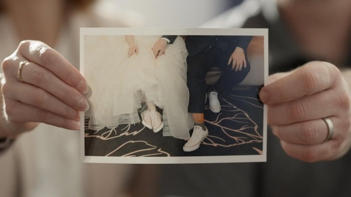 Deux mains tenant une photo montrant les chaussures de deux mariés, des espadrilles.