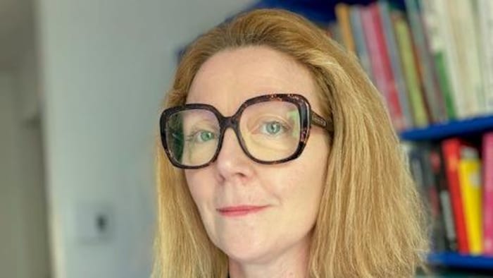 Isabelle Rivoal pose devant une bibliothèque.