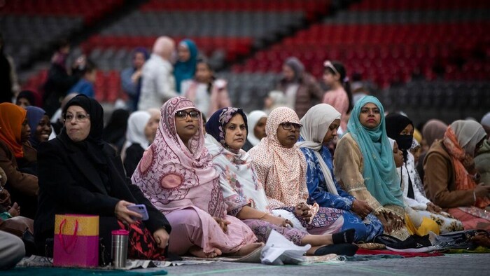 Desfemmes voilées sont assises sur différents tapis, sur le sol d'un stade.