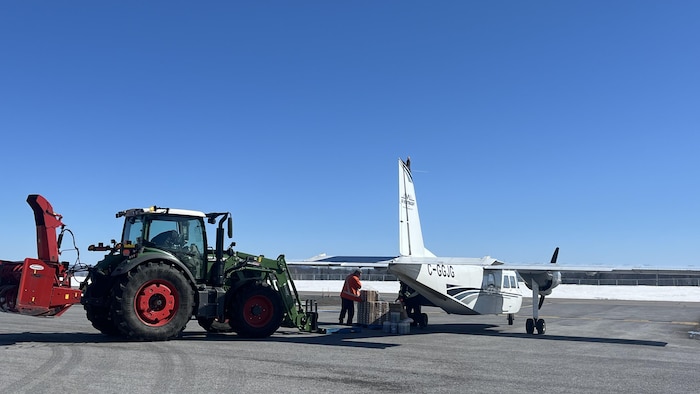 Un homme, en tracteur, dépose au pied d'un avion pour une livraison.