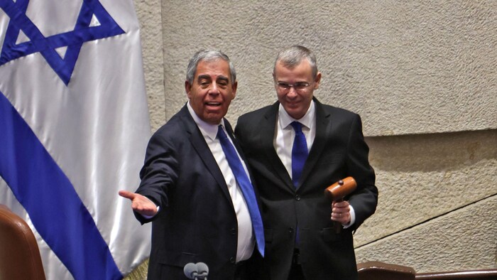 Yariv Levin est debout avec un autre homme devant un drapeau israélien.