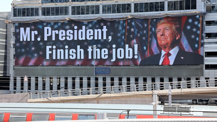 Une banderole géante sur laquelle il y a une photo du président Donald Trump avec cette phrase : «M. Le président, finissez le travail!»