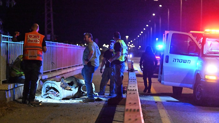 Quatre membres des forces de sécurité israéliennes examinent un fragment d'un missile iranien sur un trottoir le long d'une route la nuit.