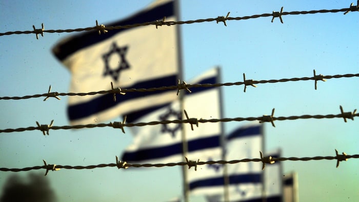 Des drapeaux israéliens flottent au vent derrière des fils barbelés.