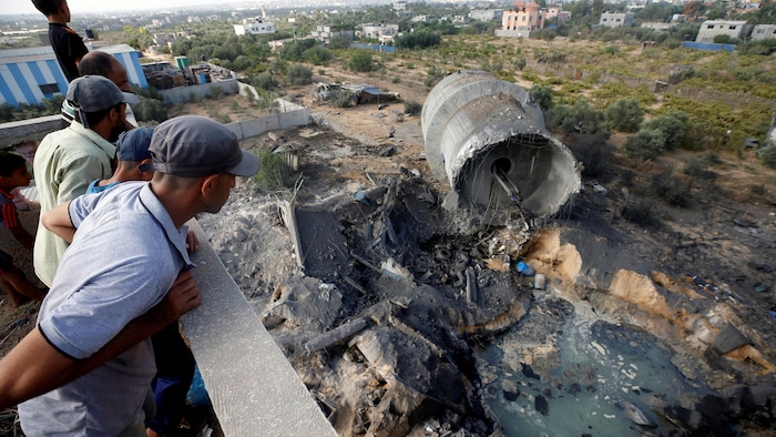 Quelques Palestiniens penchés au-dessus d'un mur observent des débris, près d'un cratère rempli d'eau.