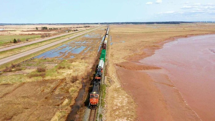 Un train circule sur une voie ferrée près d'une autoroute et tout près de l'eau.