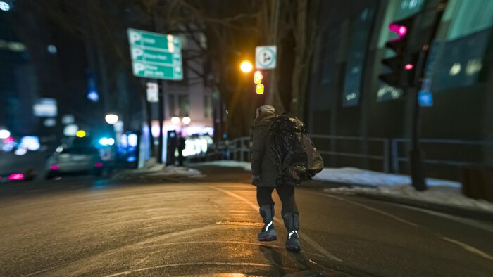 Un sans-abri traverse une rue la nuit tombée.