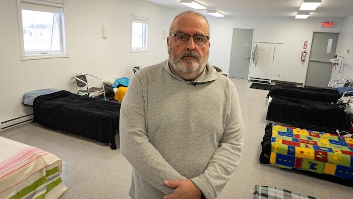 Un homme au milieu d'une pièce où plusieurs lits sont visibles.