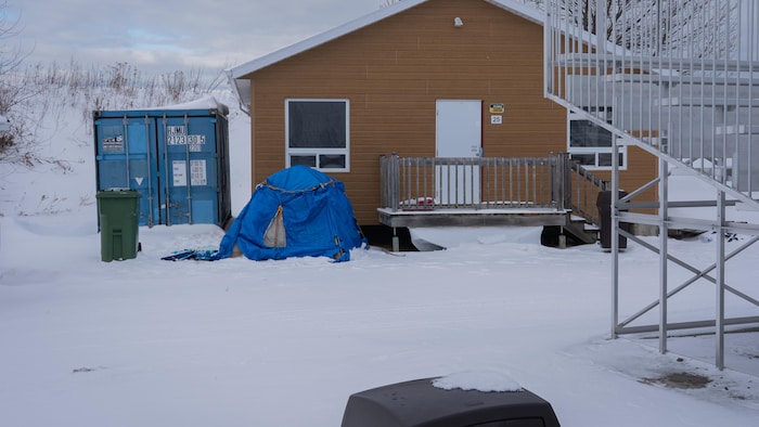 Une tente bleue posée sur la neige devant un bâtiment.