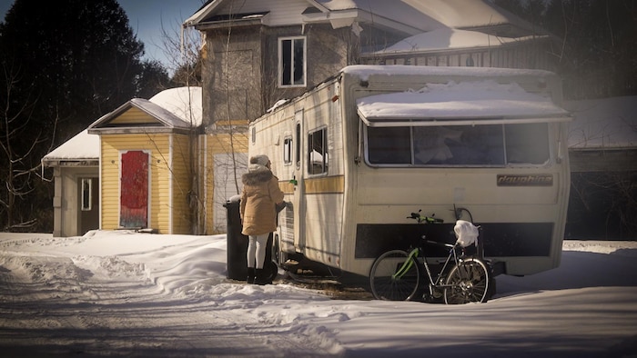 Une femme à la porte d'une roulotte dans la neige. 