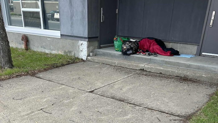 Une personne dort dans un sac de couchage sur le sol d'une entrée à Rouyn-Noranda.