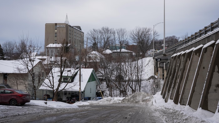 Une rue enneigée avec un viaduc, des maisons et un hôtel.