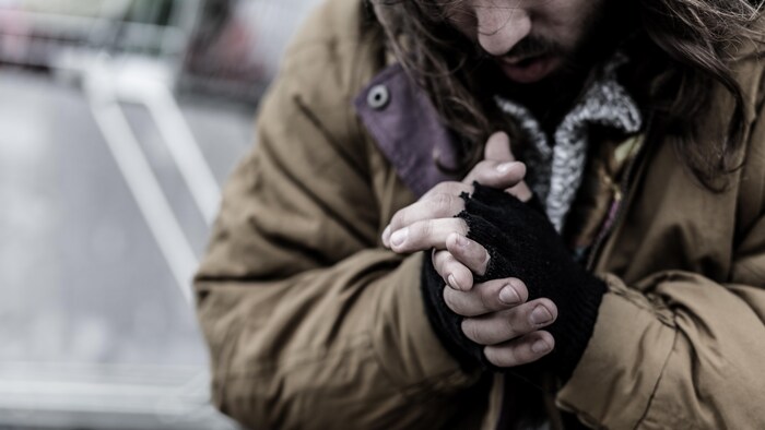 Un homme sur un trottoir se frotte les mains pour se réchauffer. 