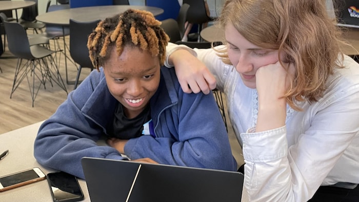 Deux élèves regardent un ordinateur, l'une s'appuyant sur l'épaule de l'autre.